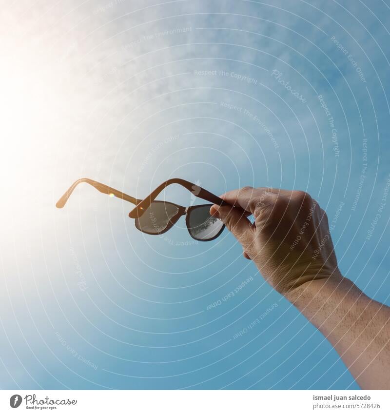 hand holding a sunglasses and blue sky background arm fingers hand up arm up hand raised arm raised skin palm palm of hand body part sunlight flare lens flare