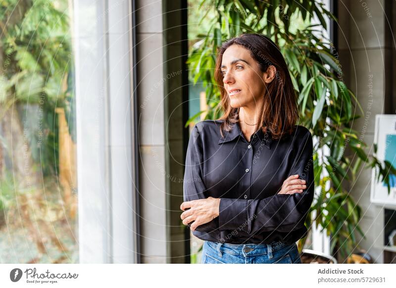 Confident Businesswoman in Modern Office Setting businesswoman entrepreneur confident looking away office contemporary plant indoor professional arms crossed