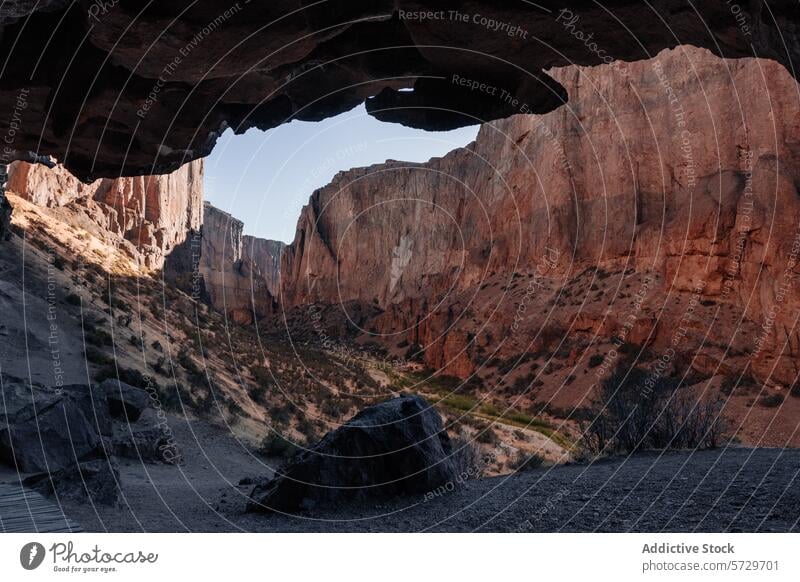 View from the shadowed interior of a cave framing the sunlit red cliffs of a Patagonian canyon, evoking a sense of remote wilderness view Argentina summer