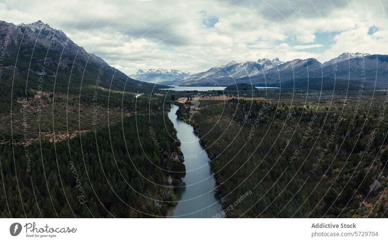 Aerial view of a tranquil river winding through a lush Patagonian valley, flanked by dense forests and the majestic Andes in the background aerial view