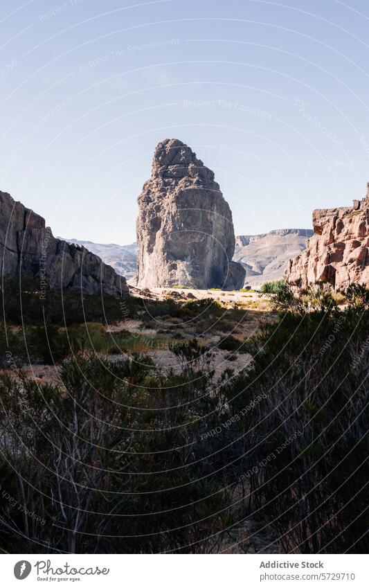 An imposing natural rock monolith stands tall amidst the rugged cliffs of a serene Patagonian valley, under the clear blue sky landscape Argentina summer