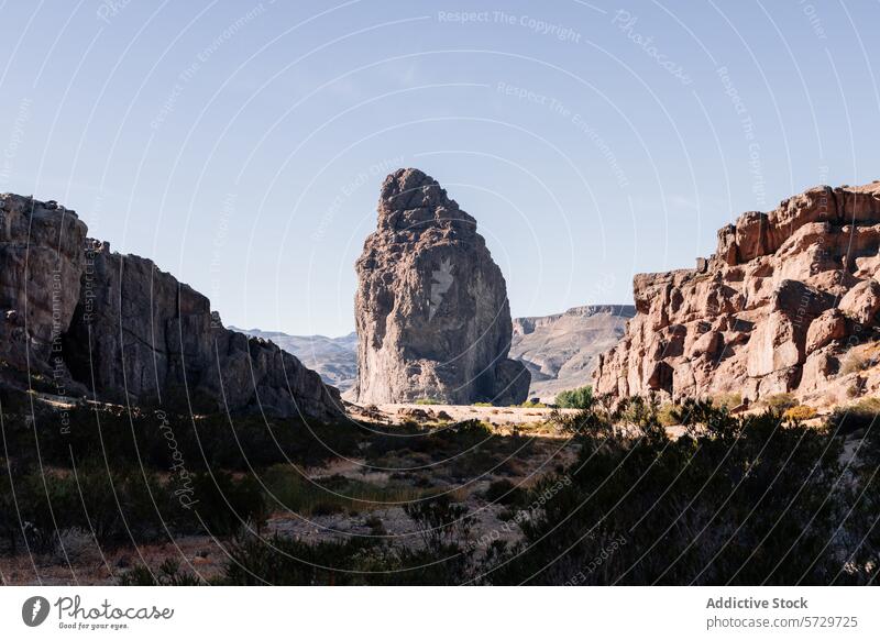 An imposing natural rock monolith stands tall amidst the rugged cliffs of a serene Patagonian valley, under the clear blue sky landscape Argentina summer