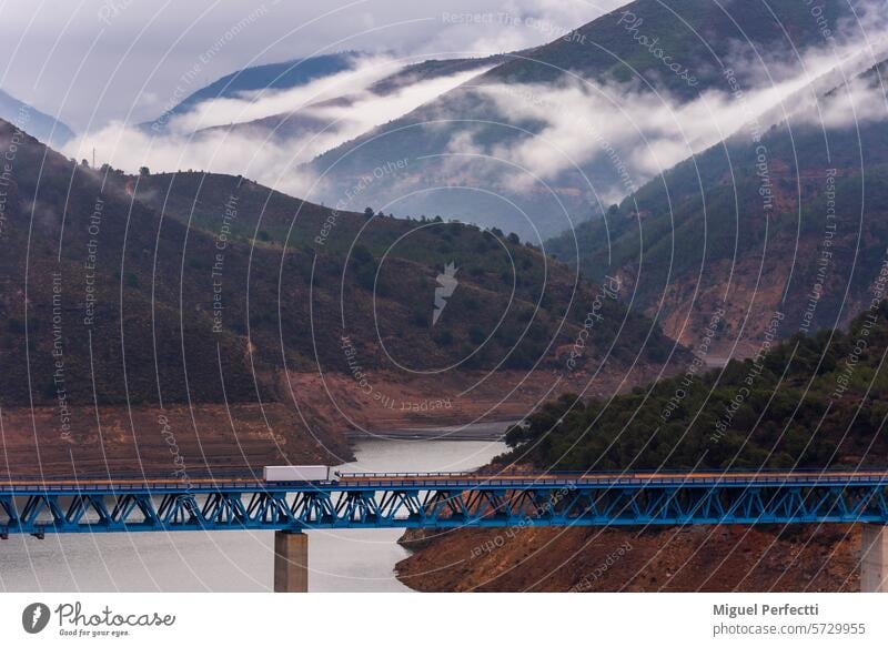 Truck with a refrigerated semi-trailer driving on a bridge over a swamp and a mountain landscape with low clouds in the background. truck transport viaduct