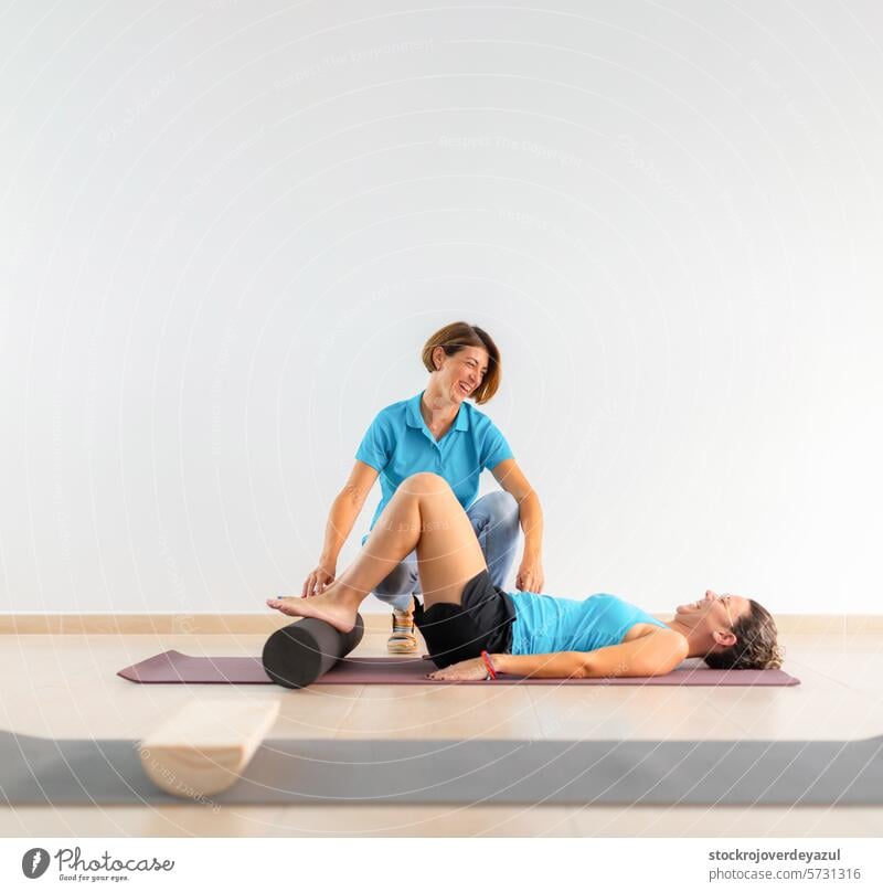 A physiotherapist helps a patient, lying on the floor, during a therapeutic Pilates workout session coach clinic rehabilitation physiotherapy exercise fitness