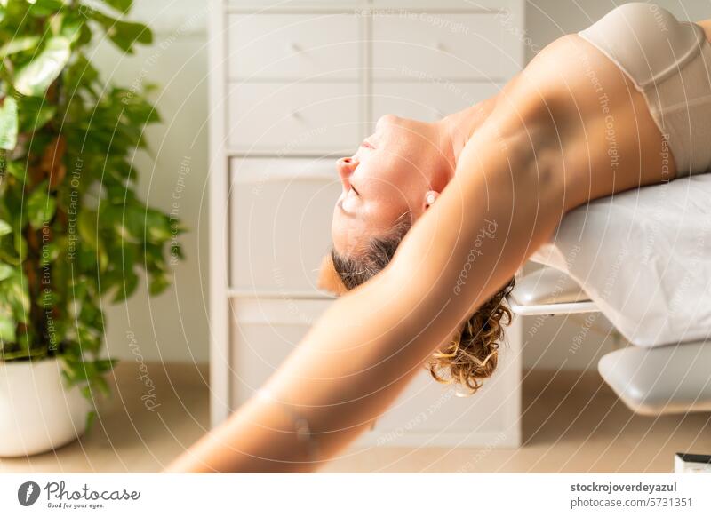 A woman performs a relaxing arm, back, and shoulder stretching exercise lying on a table at a physical therapy clinic physiotherapist rehabilitation patient