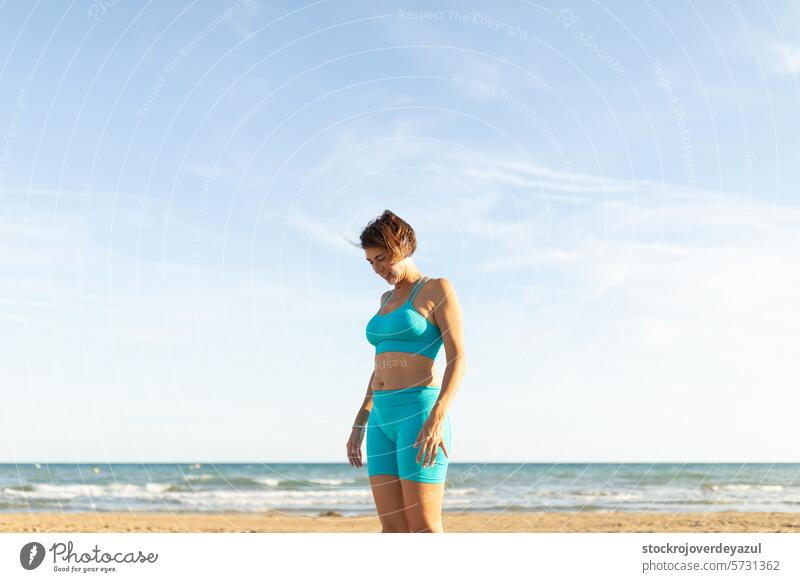 A woman rests after performing Pilates exercises on the beach, facing the sea pilates yoga mediterranean spain mind-body exercise contrology sunset real people