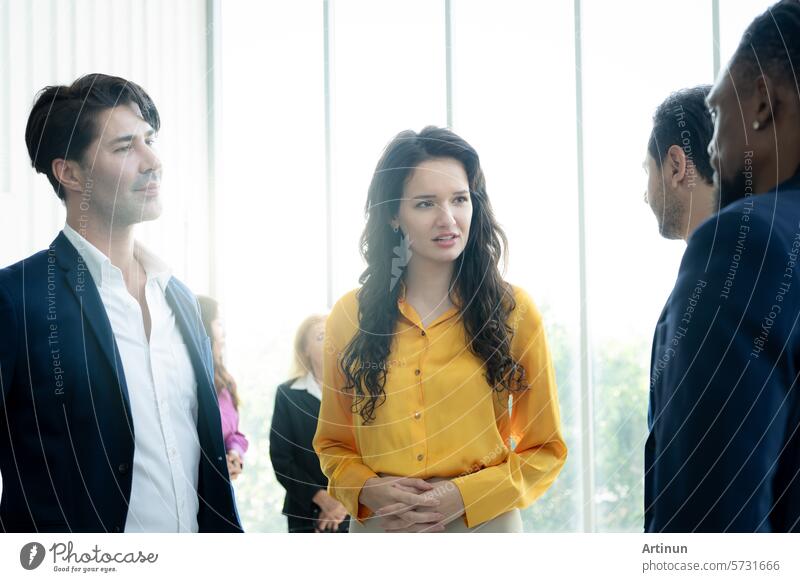 A group of people are standing in a room, one of them is wearing a yellow shirt. The woman in the yellow shirt is looking at the camera with a frown on her face