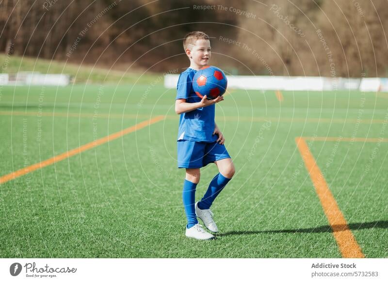 Young soccer player holding a ball on the field boy sport young uniform blue green grass standing confidence child outdoor team leisure game daytime