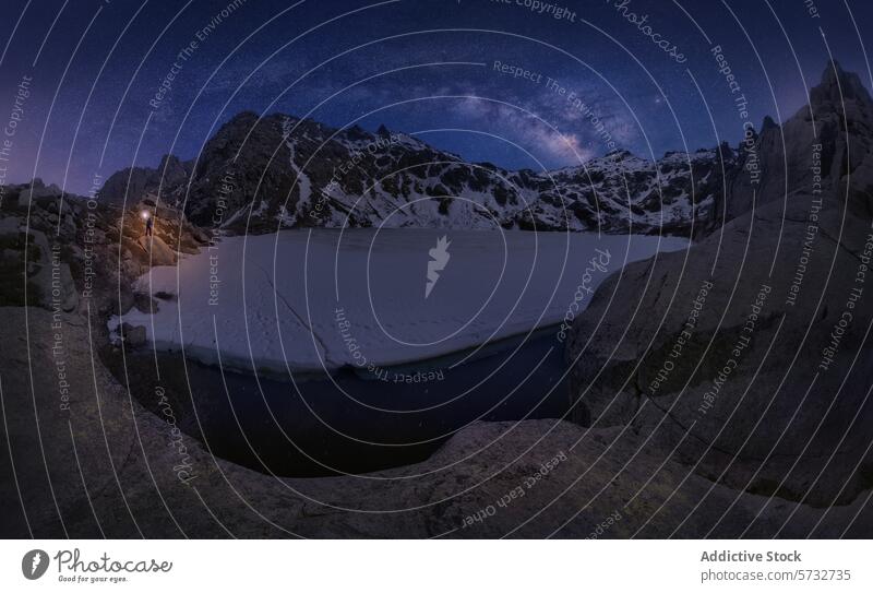 A majestic star-studded sky blankets a frozen mountain lake in Corsica, France, with a solitary hiker illuminating the tranquil scene starry night snow