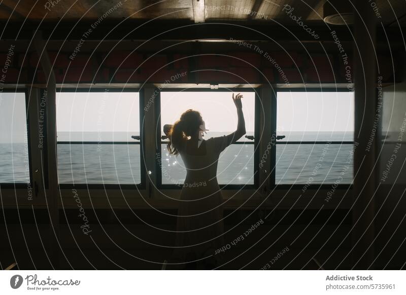 Woman in Silhouette Inside Ferry Reaching Towards Sunlight woman silhouette ferry sunlight ocean window reaching sea travel journey maritime transportation