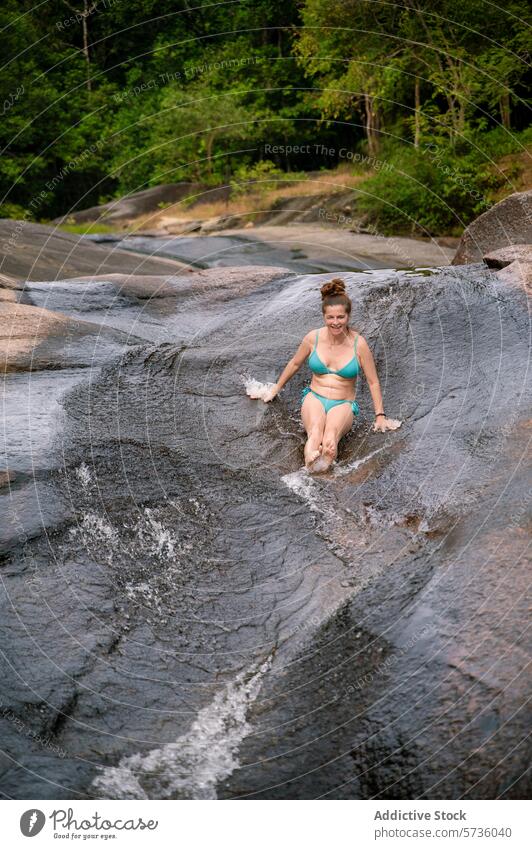 A woman glides with joy down a smooth, natural rock slide in the verdant forests of Langkawi, embracing the fun of nature river outdoor swimwear tropical