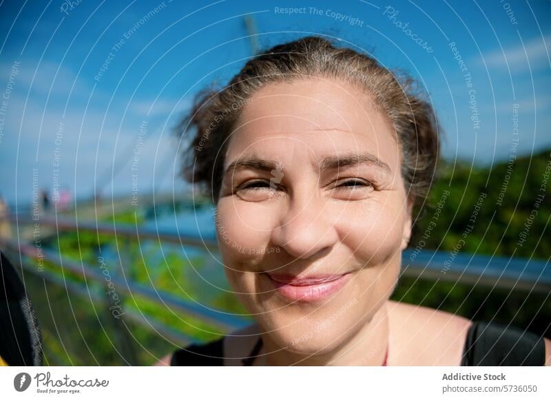 A joyful woman squints and smiles warmly under the bright sunlight at the Langkawi Sky Bridge in Malaysia sky bridge outdoor happy portrait travel tourism