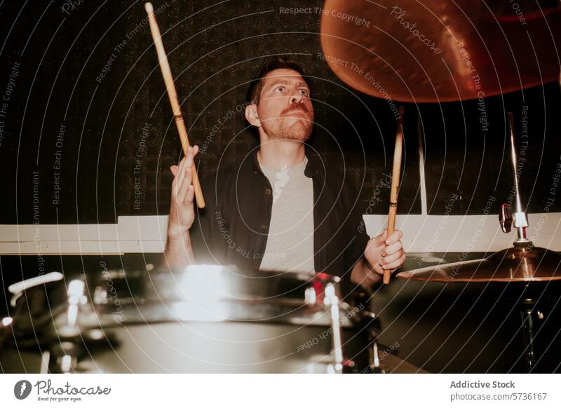 Concentrated male drummer playing in low light setting drumstick man music band instrument performance focus concentration looking away cymbal male musician