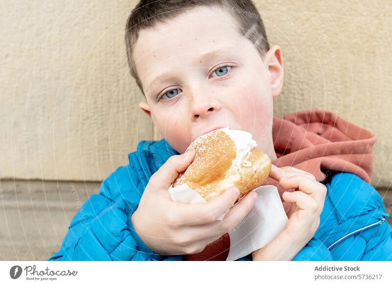 Young boy enjoying a tasty cream-filled pastry eating snack sweet child hunger treat food dessert enjoyment taste indulgence sugar powdered face eyes blue bite