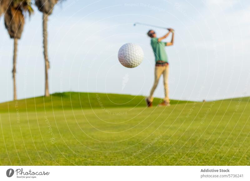 Anonymous golfer playing on a sunny day swing course green sky clear motion sport active leisure outdoor palm tree hobby ball unique male person follow through