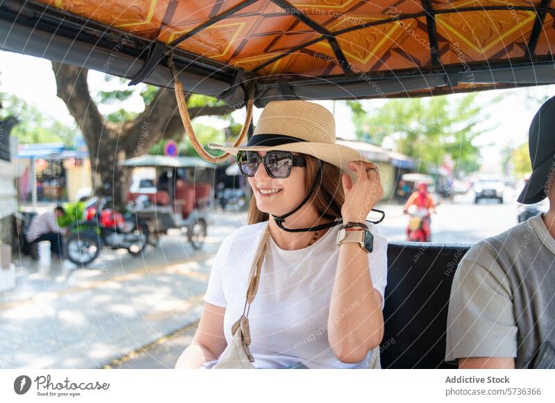 Smiling woman enjoying a tuk tuk ride on a sunny day cheerful straw hat sunglasses urban travel city blurred background transportation tourist street vacation