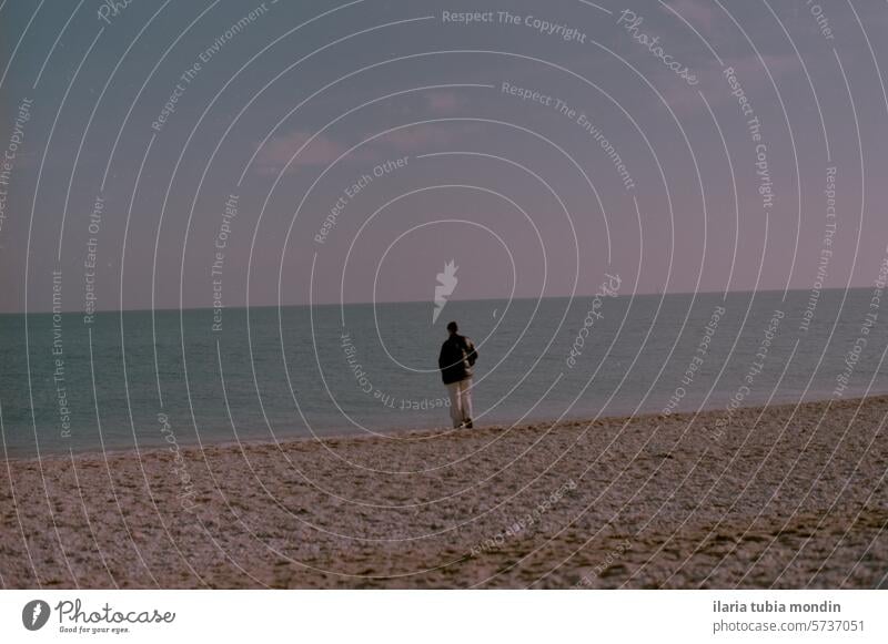 girl walking along the beach shore in winter at sunset seaside cold winter clothes blue ocean rocks sand coastline romantic purple vintage 35 mm analog kodak