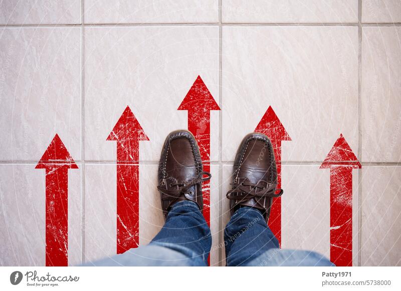 Person stands on tiled floor. View from above of the shoes/legs and the floor on which red arrows pointing the way are stuck. Arrow Footwear Legs Red Direction