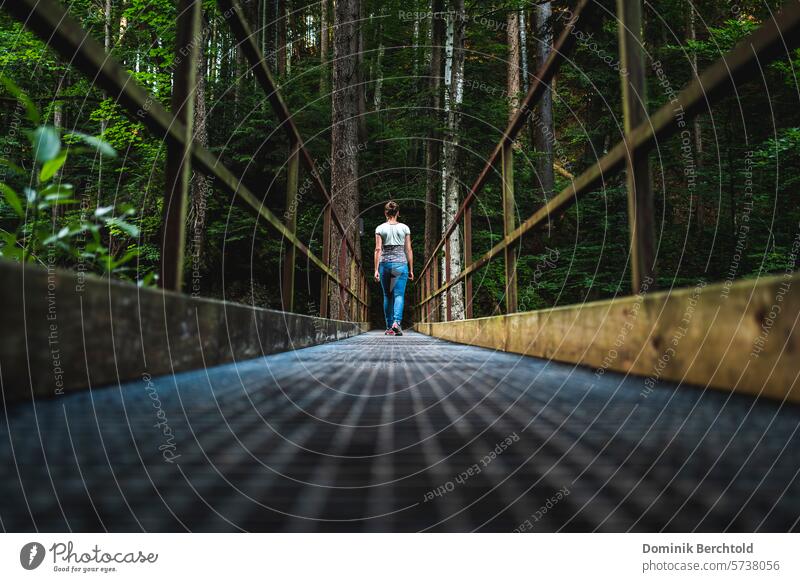 Woman crosses a bridge in the forest Summer Shadow Clouds Rain Sun mountains River Body of water trees Bridge Bridge railing Hiking hike Forest Green