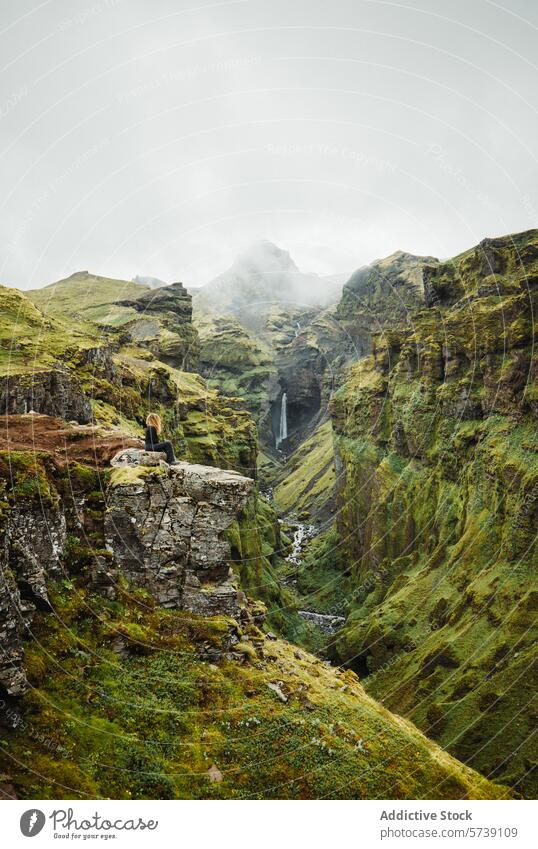 Anonymous woman sitting on cliff contemplating Nature at a Secluded Icelandic Waterfall iceland waterfall nature adventure solitude greenery landscape traveler