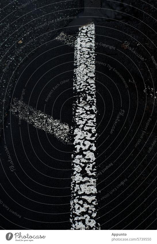 A broad white line on black asphalt. Together with other, already faded, diagonal ground markings for a so-called restricted area ("no parking"), it forms a circular sign.