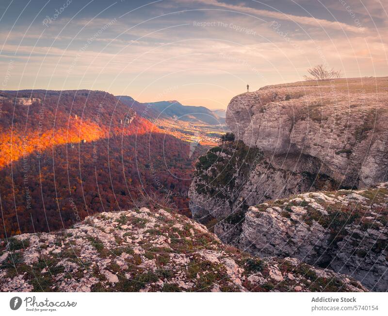 An individual stands on the precipice of the Urbasa range, gazing over the breathtaking autumnal colors of the deep gorge below at dusk figure overlook view