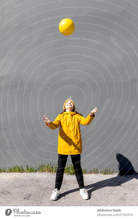 Child in Yellow Playing with Ball Outdoors child ball play outdoor yellow jacket sky clear joyful fun activity kid playful reaching bright color coordination