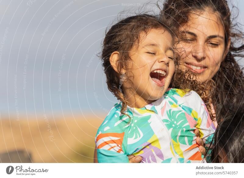 In the warm glow of the sun, a joyful child laughs heartily in her mother's loving embrace at the beach love laughter sunny family single mother girl toddler