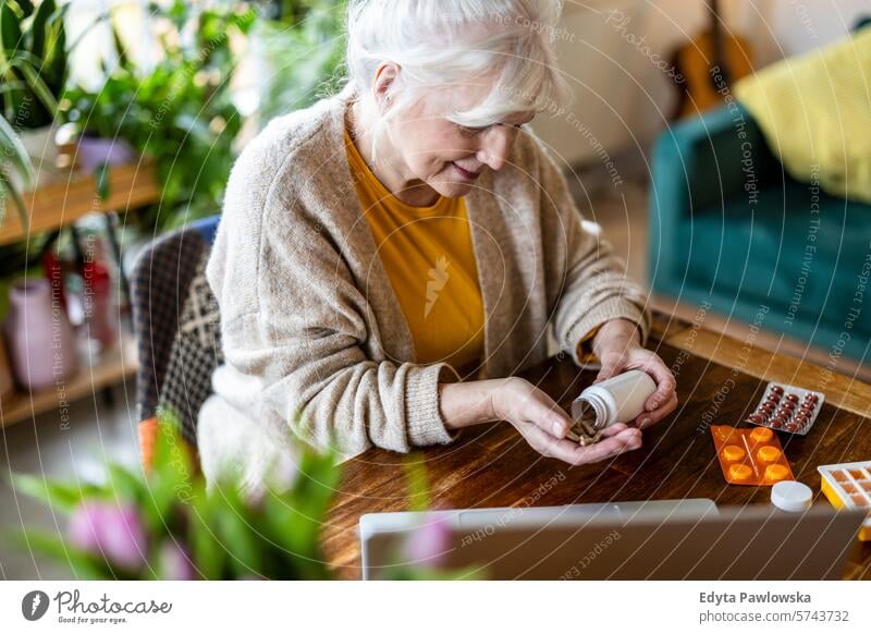 Senior woman taking pills from a bottle while sitting at the table at home people casual day portrait indoors real people white people adult mature retired old