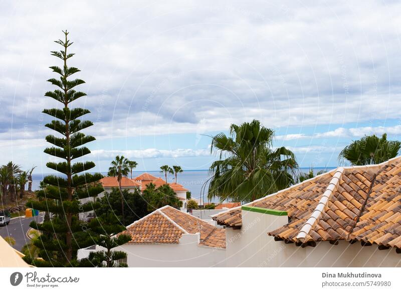 Tenerife view. Red roof tiles and green trees and palm trees with ocean aerial view with cloudy sky. tenerife island rooftop red roof tiles Roof Architecture