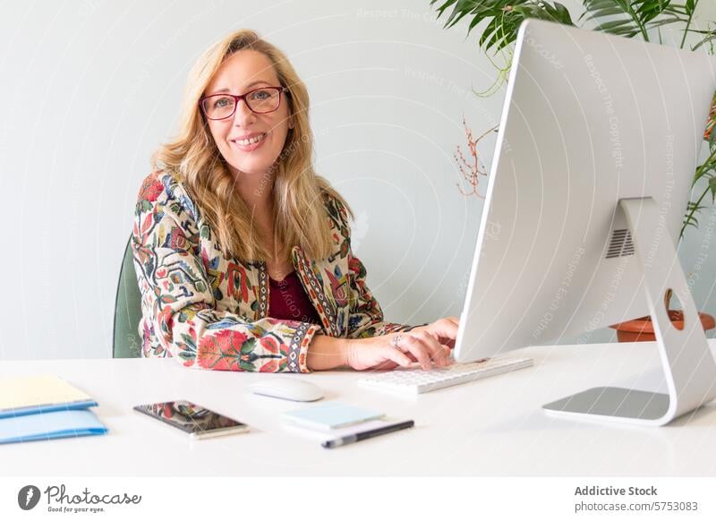 Smiling blond businesswoman working at her desk smile computer office professional glasses modern female technology keyboard screen monitor professional attire