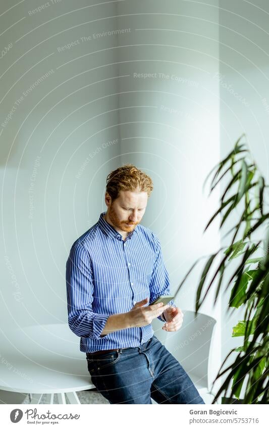 Serene Afternoon Break. Gentleman Engrossed in Smartphone Amidst Urban Indoor Greenery. adult afternoon age attire browsing calm casual column communication