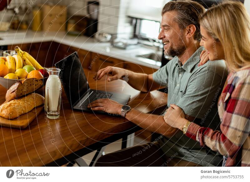 Cheerful couple enjoys a light-hearted moment in their sunny kitchen, working on laptop surrounded by a healthy breakfast adult bonding browsing casual clothing