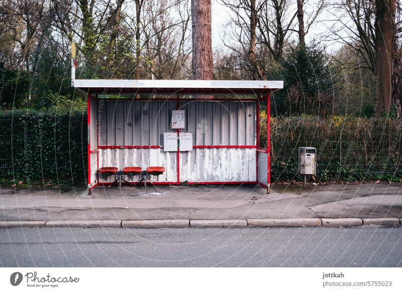 A lonely, somewhat run-down, empty bus stop on a sidewalk in front of a hedge and forest Bus Stop (public transport) Bus stop Transport Public transit