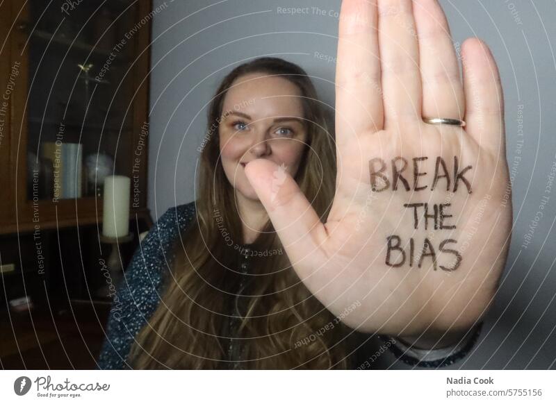 Young female in background holding up hand in foreground with writing break the bias written on palm of hand handwriting rights woman slogan womens equality