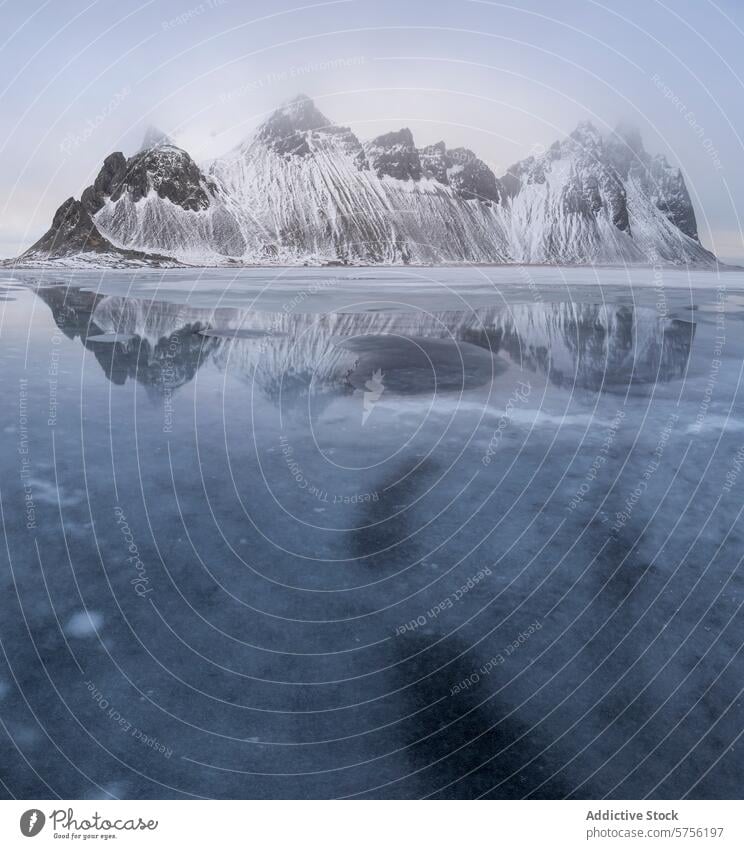 Icy Reflection of Stark Mountain Peaks in Iceland iceland mountain reflection peak snow frozen water moody sky winter glassy surface landscape nature cold