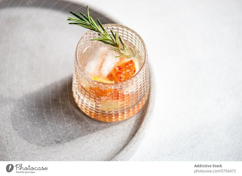 A crafted vodka tonic cocktail adorned with grapefruit and rosemary, resting on a textured tray for an upscale serving experience drink beverage ice garnish