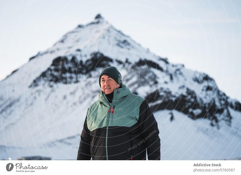 A warmly dressed man stands in the foreground, his gaze directed towards the summit of a majestic snow-covered mountain in Iceland peak travel winter outdoor