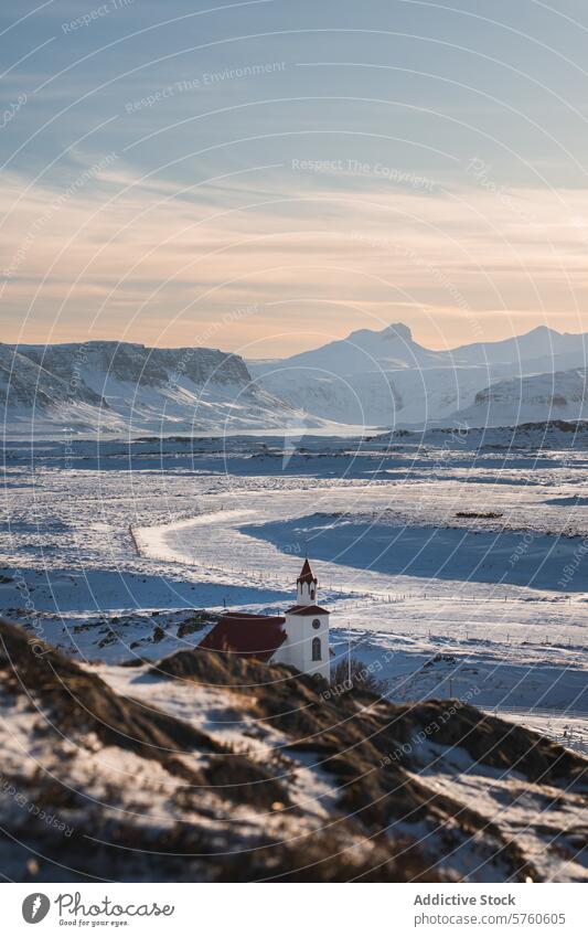 A picturesque white church with a red roof stands out in the expansive, snow-covered landscape of Iceland, with majestic mountains under a clear sky Icelandic