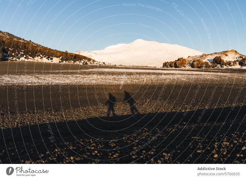 Two silhouetted figures cast long shadows on the vast, snowy plains of Iceland, with a magnificent white mountain looming in the distance Icelandic travel