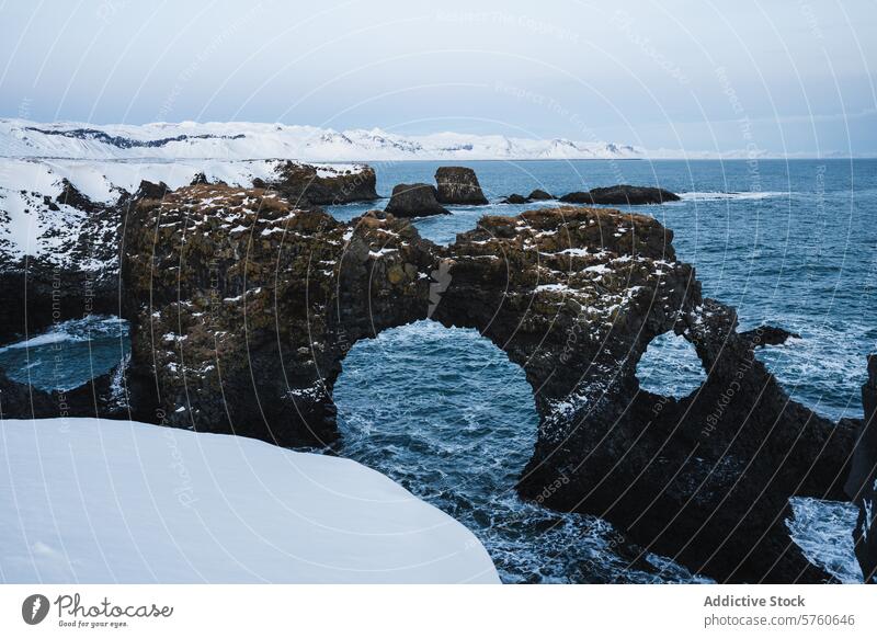 The natural arch of volcanic rock stands amidst the snow and turbulent waters along the starkly beautiful coast of Iceland winter archway Icelandic seascape