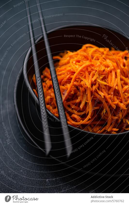 Delicious spicy Korean carrot salad in a bowl chopstick black ceramic dark close-up food cuisine vegetable side dish orange grated seasoned healthy vegan