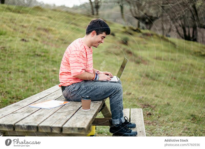 A man is deeply engrossed in his work on a laptop while seated alone at a wooden picnic table, surrounded by the tranquility of nature outdoor focused