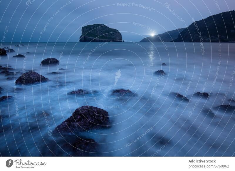 A solitary lighthouse beacon shines across the dusk-veiled waters near the rugged coast of Gaztelugatxe, Spain sea ocean night twilight rock landscape nature