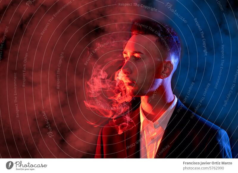 Elegant young man blowing cigarette smoke out of his mouth on a black background. Selective focus businessman health suit person one copy space dark elegant