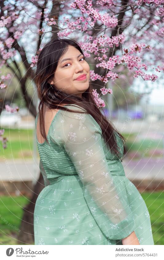 Woman in green dress enjoying cherry blossom season woman spring casual sneakers park nature outdoors blooming tree grass leisure floral fashion lifestyle