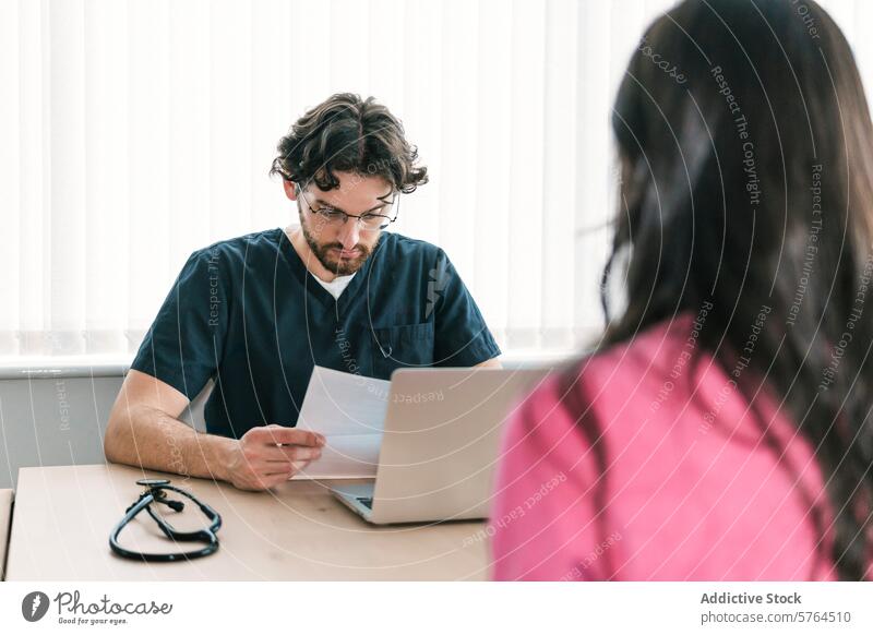 A doctor is intently reviewing documents during a patient appointment, exemplifying meticulous care in patient treatment focused healthcare medical scrubs