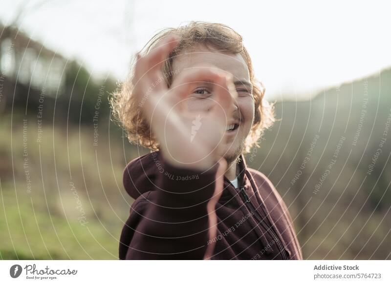 A man makes a playful gesture with his hand, creating a visual frame for his face, as he smiles during the warm, golden hour of sunset joy casual nature outdoor