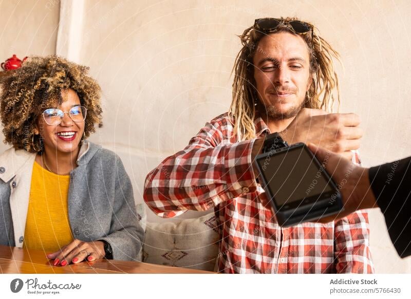 Joyful Friends Sharing Payment at a Cozy Bar rasta black woman afro multiethnic afro hair joy friends payment smartwatch contactless bar fun laughter