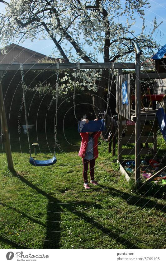 a small child hides behind a swing in the garden To swing Swing Child Infancy Joy Garden pink Spring sunny Playing Movement Joie de vivre (Vitality)